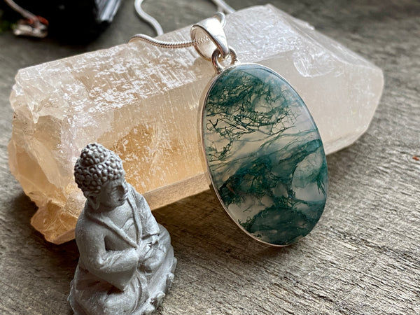 Green Moss Agate Silver Pendant in front of a citrine point and next to a small buddha statue